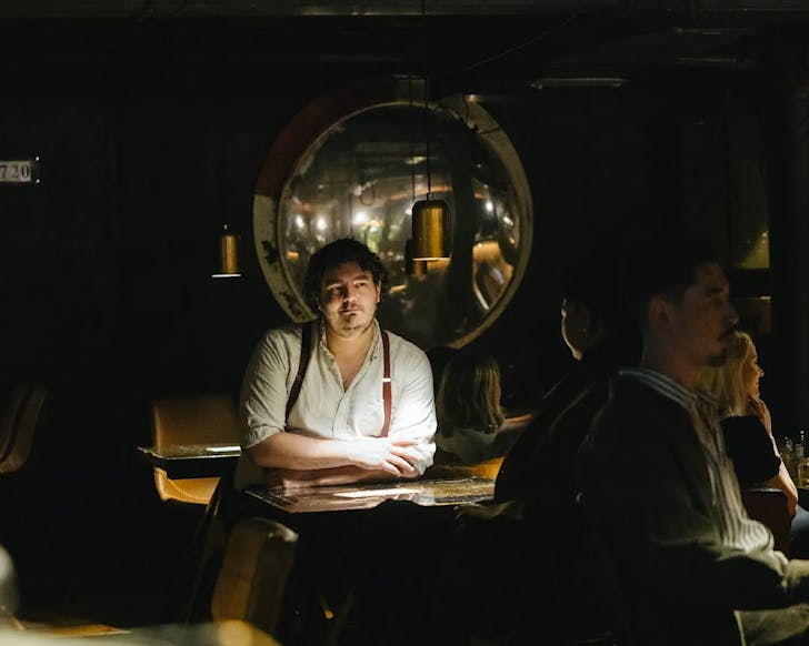 Two men sit at a dimly-lit table at Caretaker. 