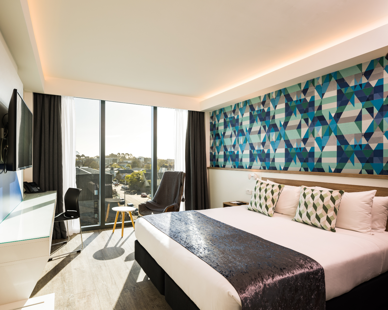 Drenched in sun, a room at the Carnmore Hotel features colourful art, a plush bed, and city views 