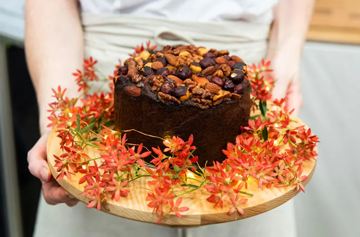 A person holding a Christmas cake decorated with flowers. 