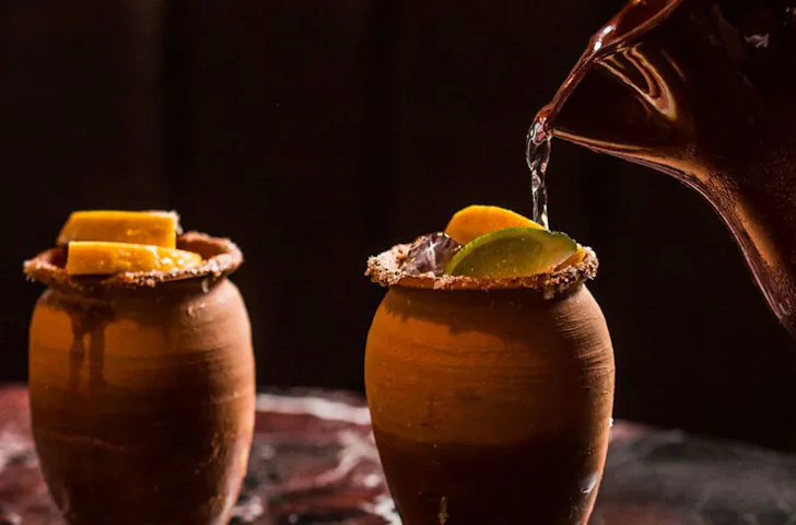 Cocktail being poured from a copper jug into stoneware cups. 