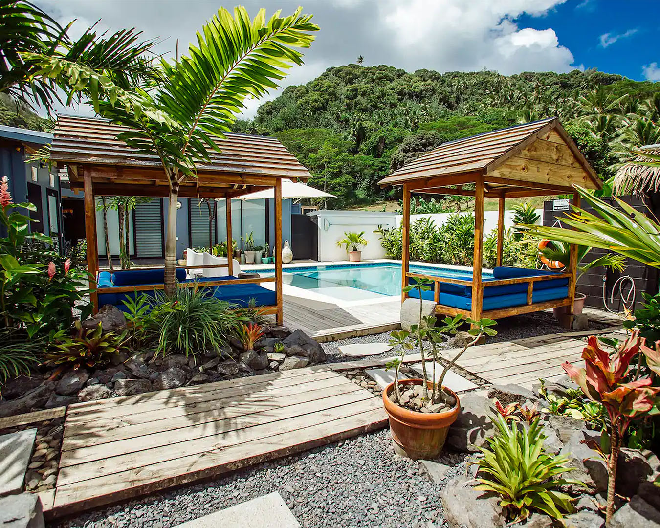 Day beds surround a lush pool amongst greenery in this airbnb in Raro.