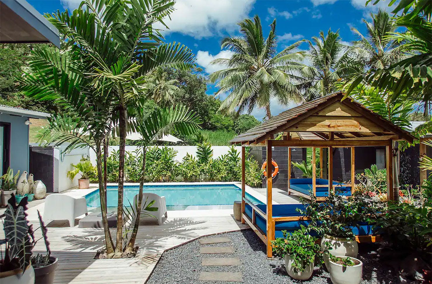 Day beds surround a lush pool amongst greenery in this airbnb in Raro.