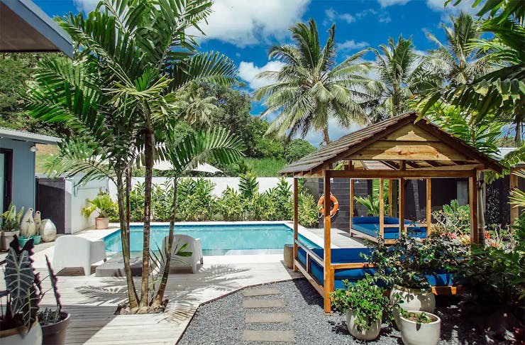 Day beds surround a lush pool amongst greenery in this airbnb in Raro.