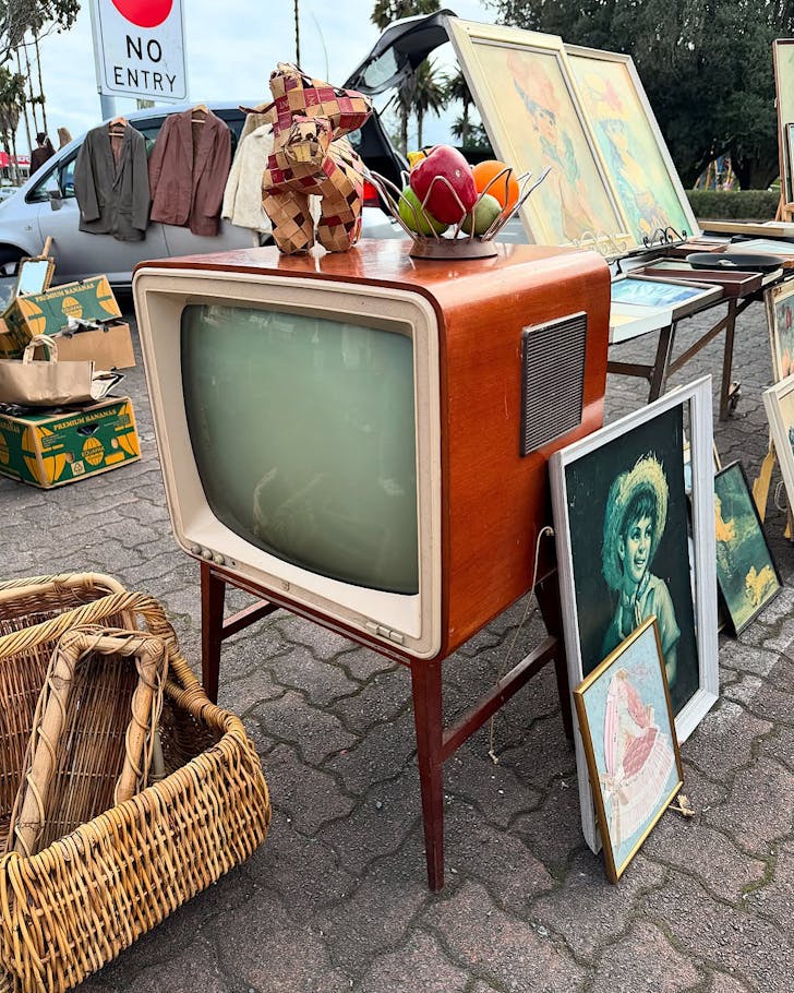 An assortment of vintage items, such as a retro TV and paintings, stacked outside and ready for sale at Central Flea.