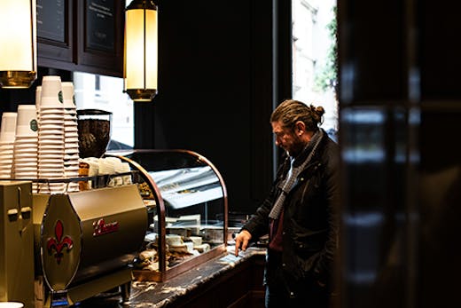 A man standing next to a coffee machine in a moody cafe.