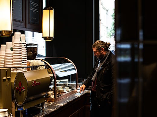 A man standing next to a coffee machine in a moody cafe.