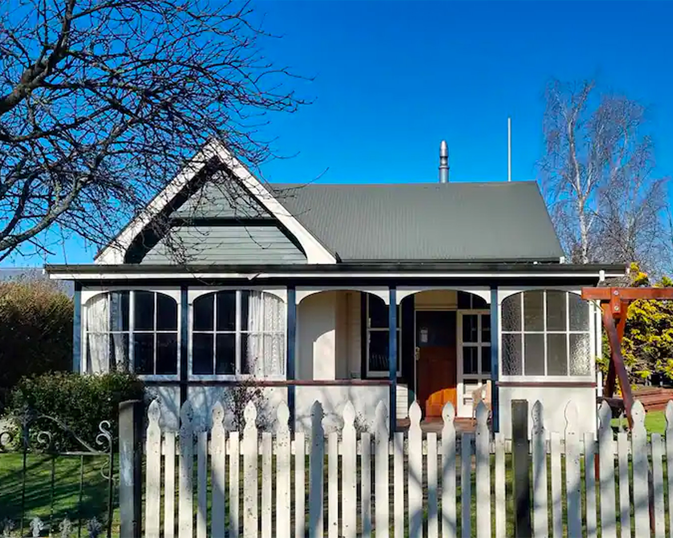 A white, classic silhouette villa sits behind a white picket fence, under a clear blue sky in one of the best spots to stay in Hanmer Springs. 