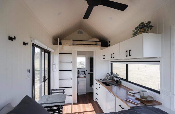 the inside of a tiny house, with a loft bed and kitchen