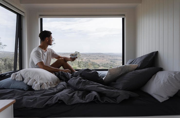 a person in a bed with windows overlooking a scenic view