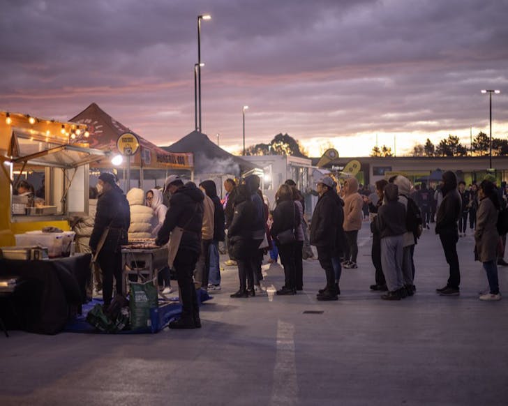 Rugged up people line up for a food stall on a chill night as sunset.