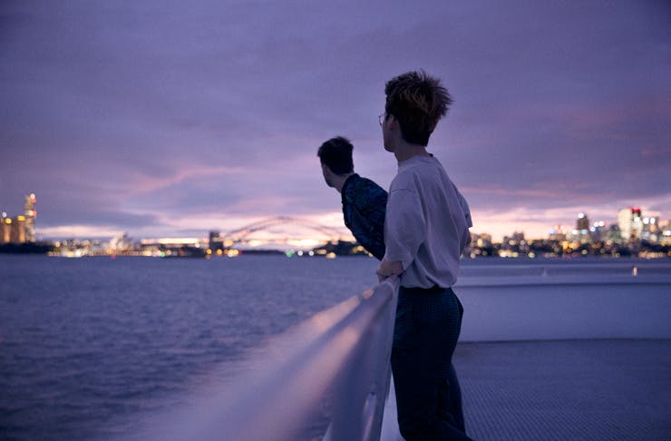A couple on the roof of a ferry, with Sydney Harbour at dusk in the background. 