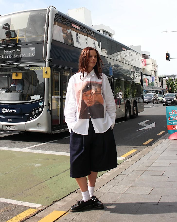 Check co-store manager Piper poses in Checks clothing in front of a busy road with an Auckland Transport bus driving by.