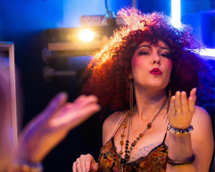A cast member of Chicago The Musical is all dolled up and blows a kiss to the camera, in a blue room.