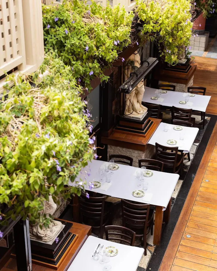 Open-air dining courtyard with white table settings, classical statues and cascading greenery inside Ettalong Galleria on the Central Coast.