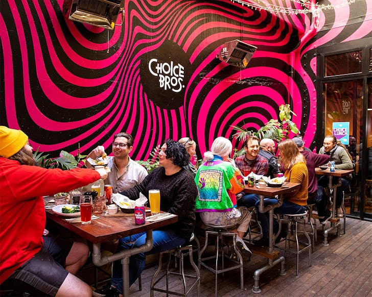 People revelling at Choice Bros at tables eating and drinking with a cool psychedelic mural on the wall.