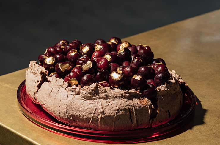 A chocolate pavlova on a table covered in cherries.