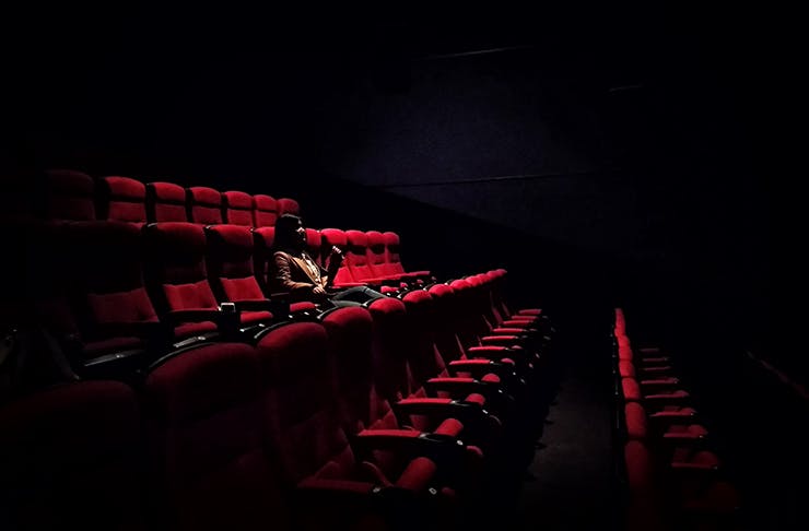 Woman sitting in dark cinema eating a choc top.