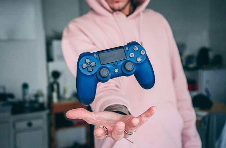 a man in a pink hoodie holds out a gaming control