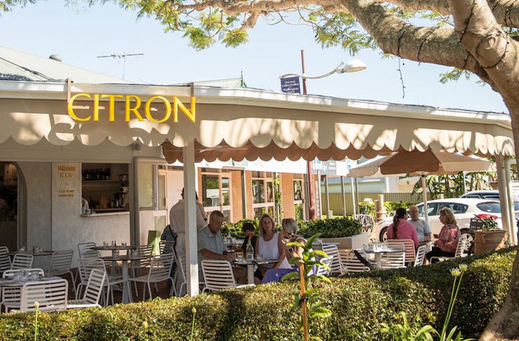 citron as seen from the street, with an outdoor dining area with umbrellas under a large tree