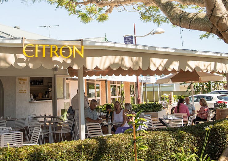 citron as seen from the street, with an outdoor dining area with umbrellas under a large tree