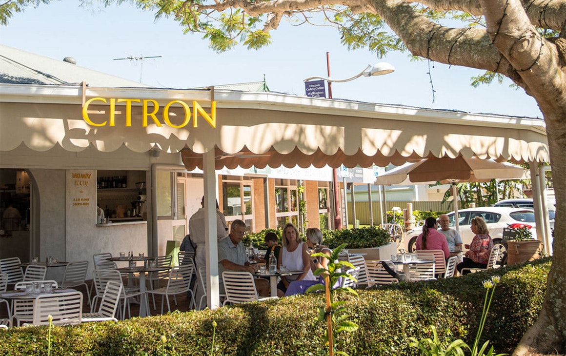 citron as seen from the street, with an outdoor dining area with umbrellas under a large tree