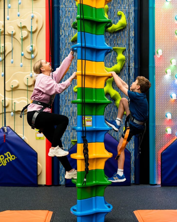 a mother and son climb a rope ladder at clip n' climb climbing gym