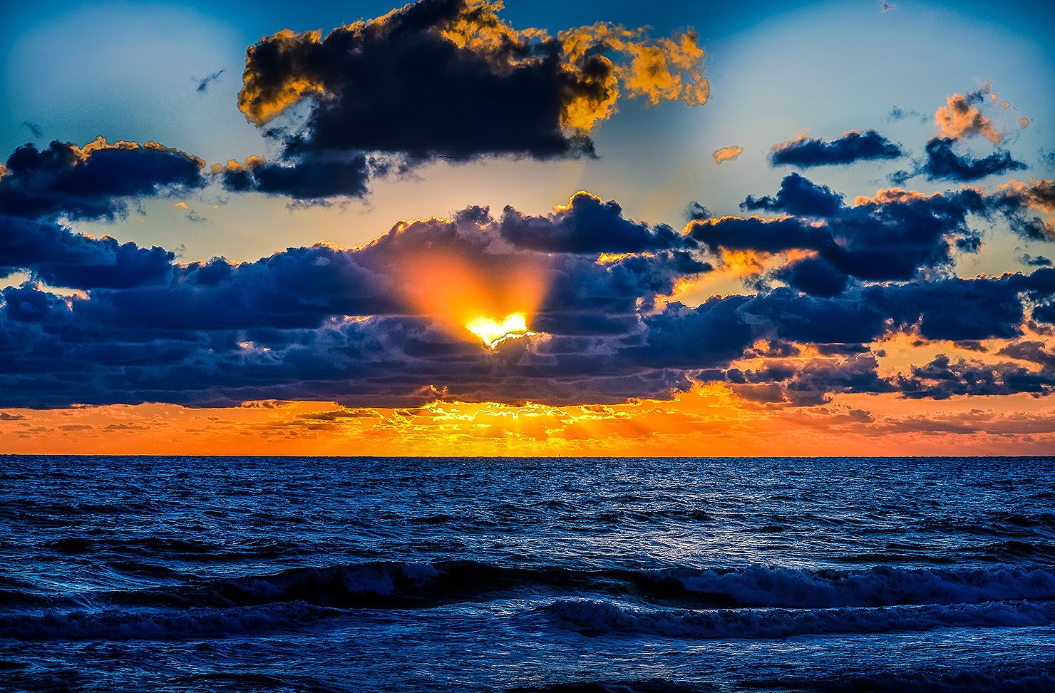 The sun peeks out behind stormy clouds, in the shape of a heart.