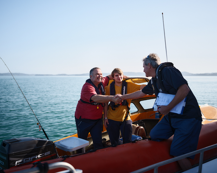 Father and son on a boat greet a CG volunteer.