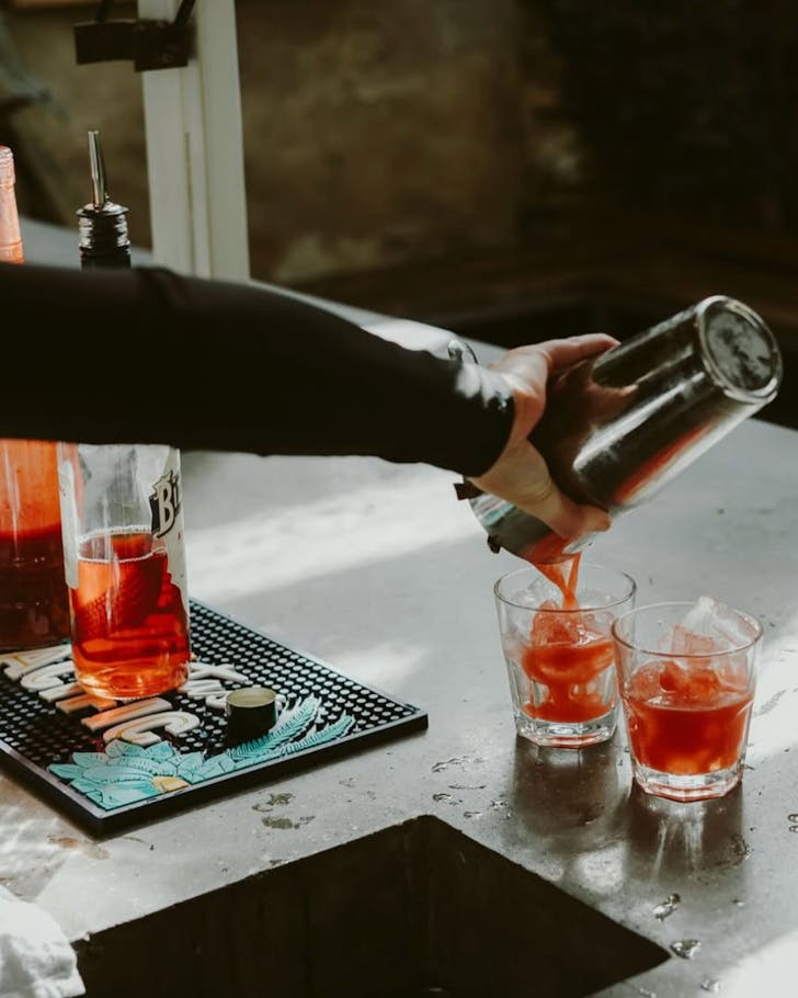 A bartender pours a bright orange cocktail.