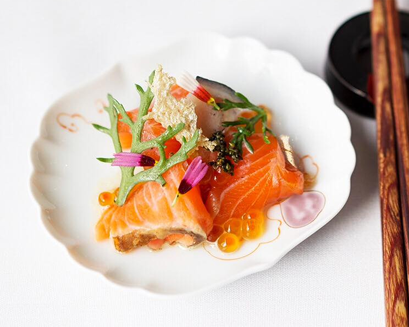 A sashimi dish sits on a white plate with chopsticks at the ready.