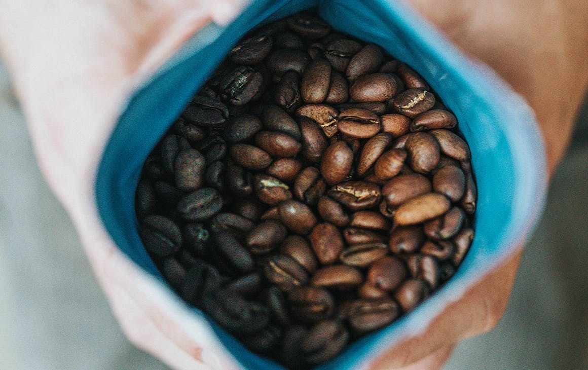 roasted coffee beans in a bag held open by a pair of hands