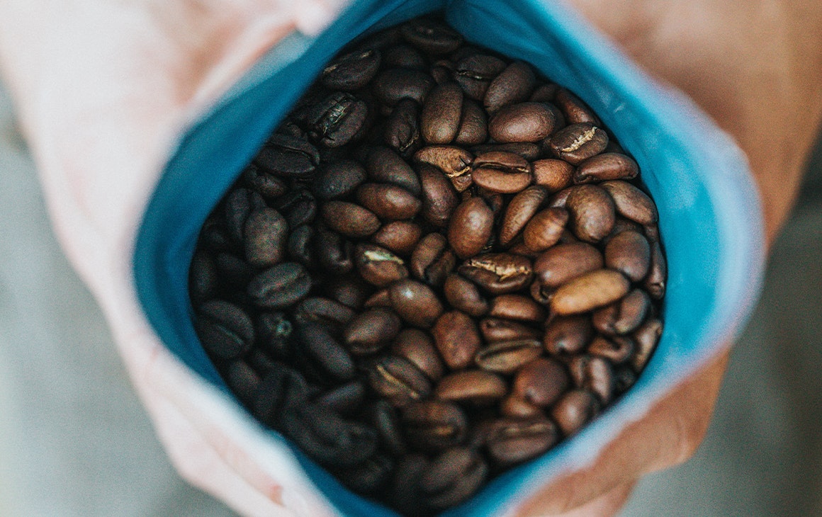 roasted coffee beans in a bag held open by a pair of hands