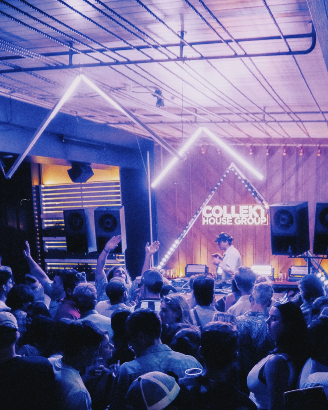 Collekt House Group play to an indoor rave with purple lights and their neon sign-written name glowing behind the solo DJ.