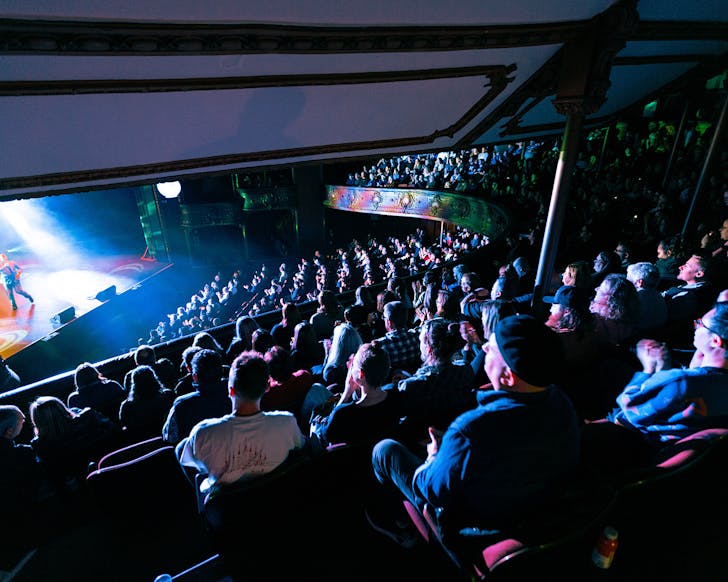 A seated crowd in an indoor amphitheatre enjoys the show.