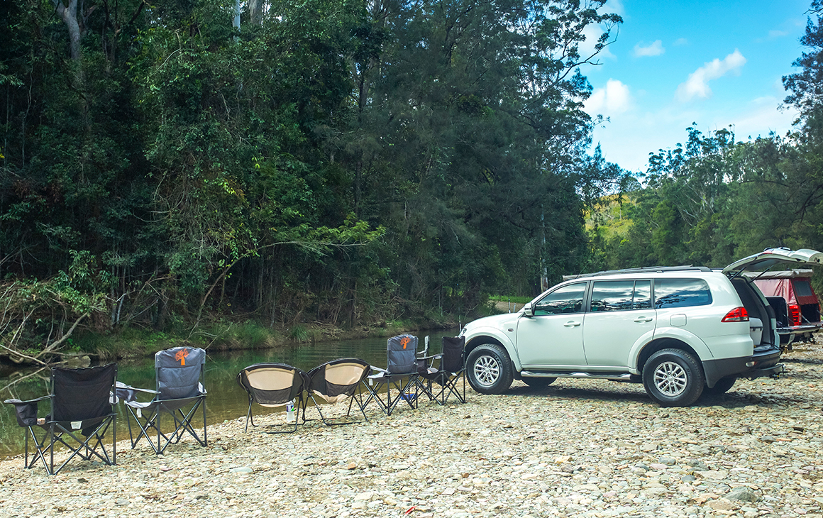 cars and camp chairs by a creek in a rainforest