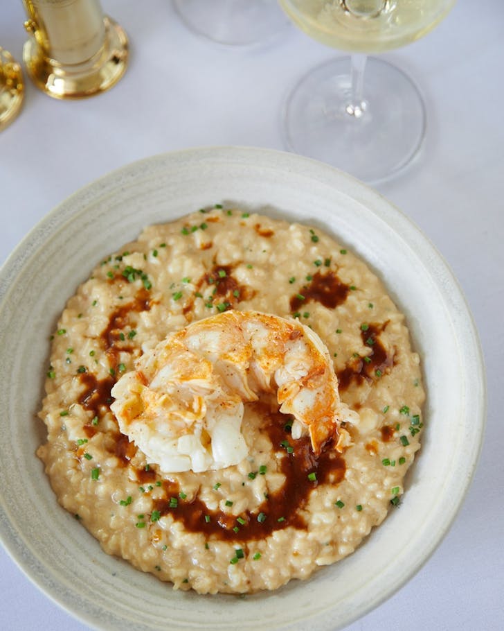 a risotto dish topped with lobster, with a glass of white wine