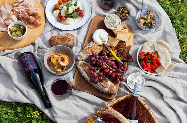 a picnic spread in the grass including several bottles of wine.