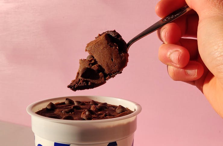 A hand dips into a cookie dough tub.