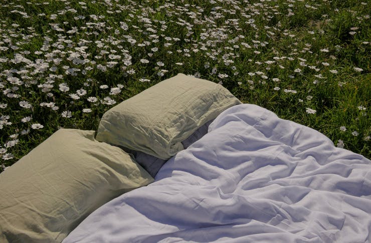 A bed with green and white sheets set up on the grass
