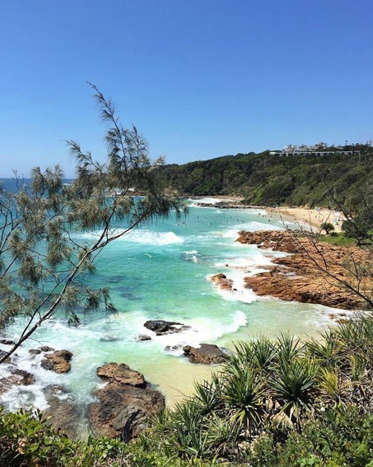 first bay beach coolum, blue skies and green waters surrounded by bushland and rocky outcrops