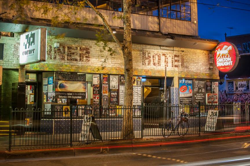 Considered one of the best pubs in Melbourne, the corner hotel sits on a busy street illuminated at night.