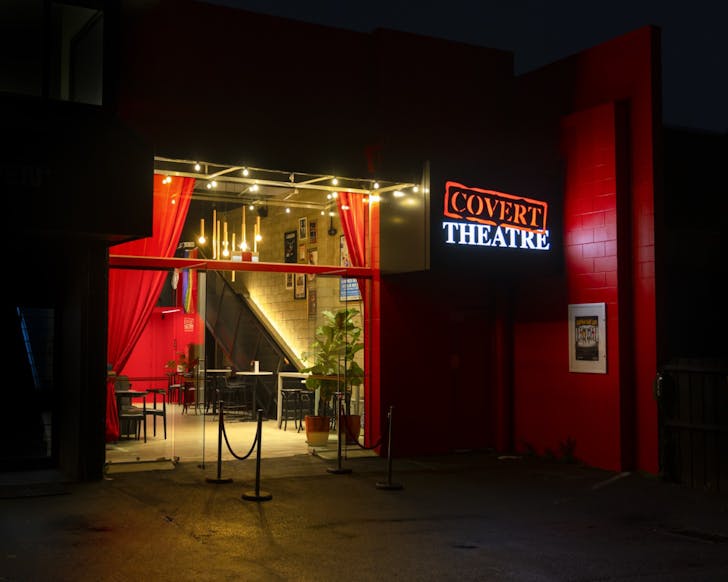 The exterior of Covert Theatre at night, with the words lit up in orange and white on a sign.