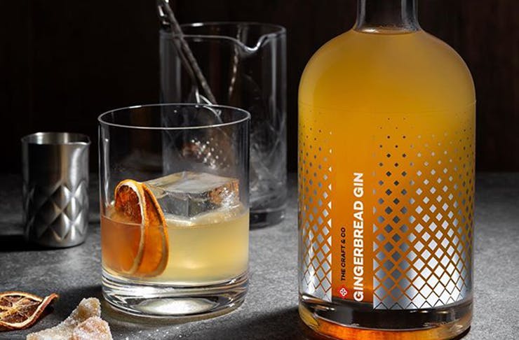 A bottle of orange coloured gingerbread gin next to a glass with citrus slices inside it.