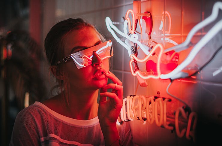 A woman in sunglasses looking at neon lights.