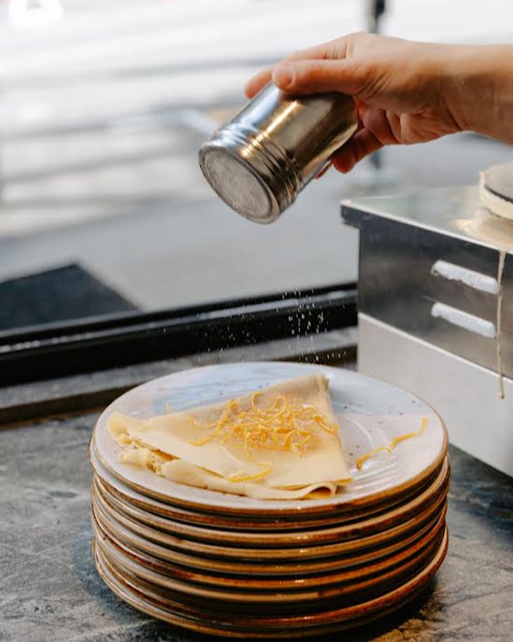Someone sifts icing sugar over a crepe folded into a triangle.