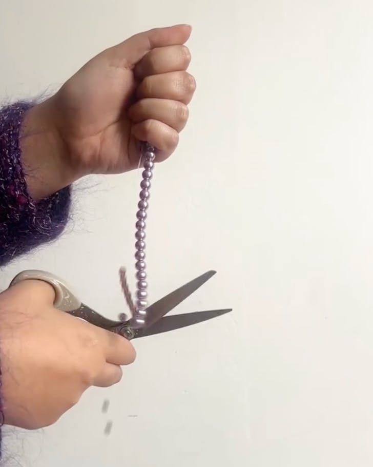 Some takes a pair of kitchen scissors to a string of shiny purple beads.
