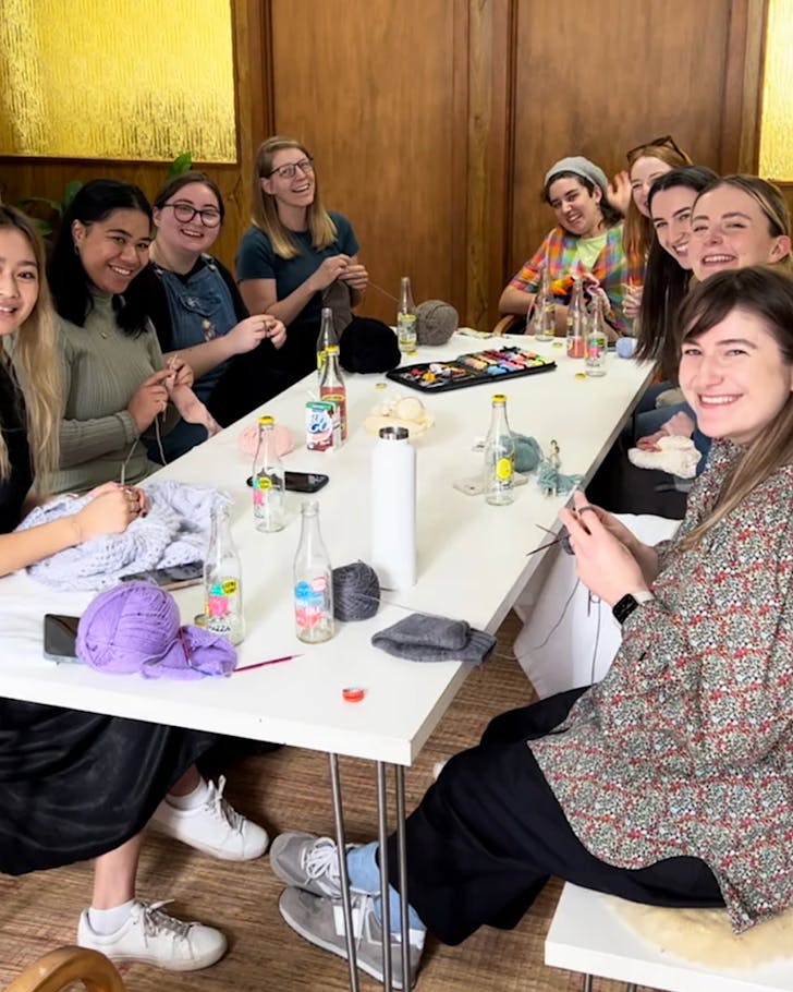 Some gals sit around a table, enjoying knitting club as part of Crushes Social Club.