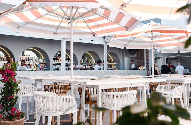 An image of a rooftop bar with high tables and striped umbrellas.