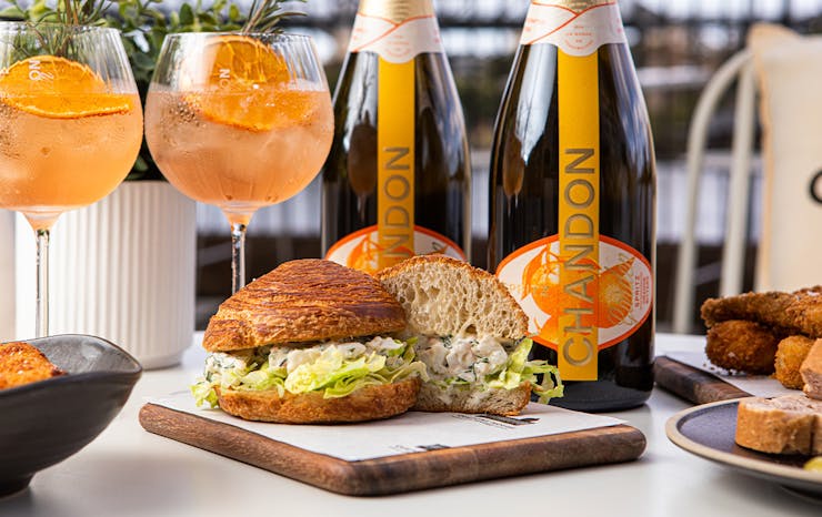 a croissant roll on a board in front of bottles and glasses of Chandon Garden Spritz