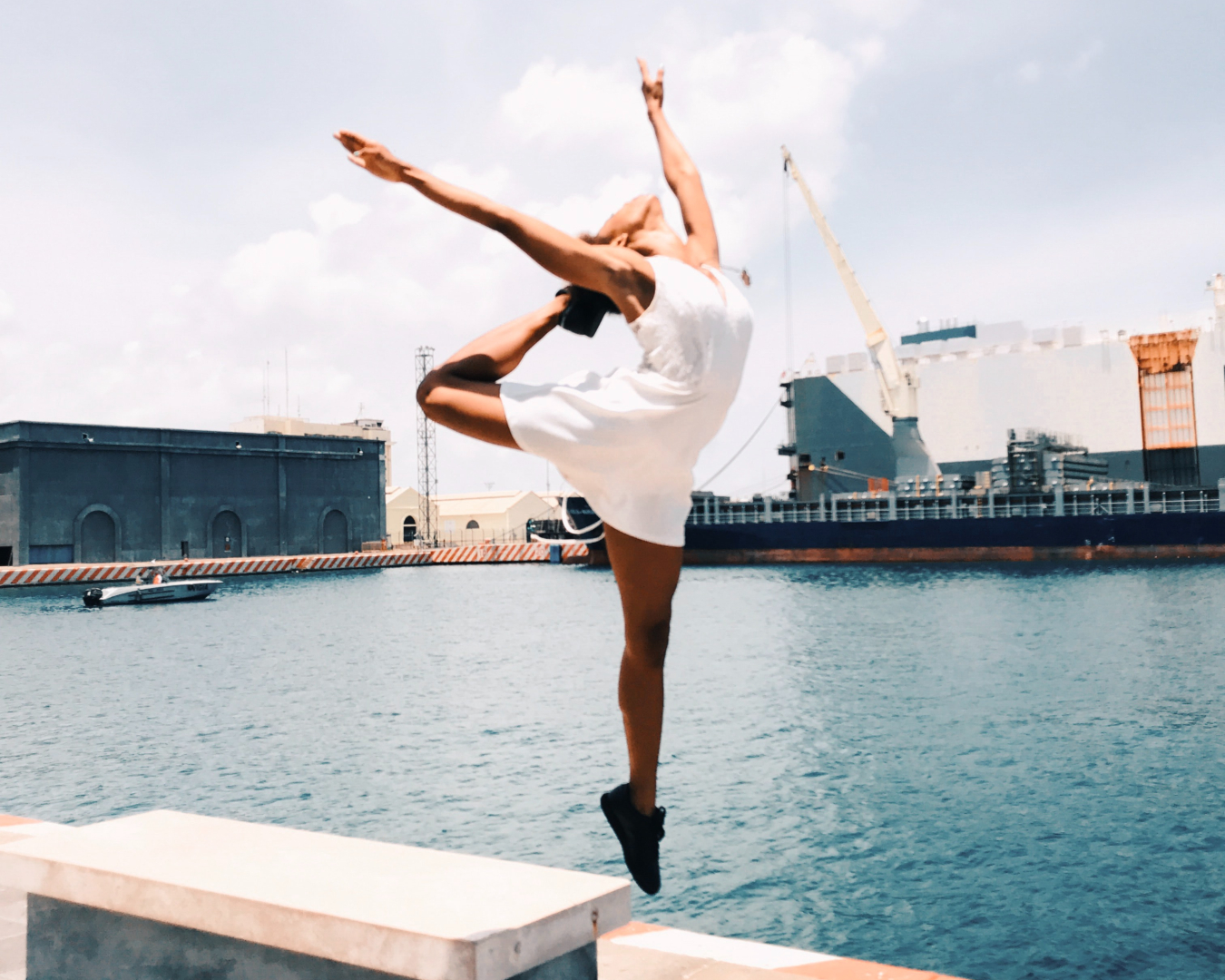 Woman jumping in mid-air with arms high, next to a city port